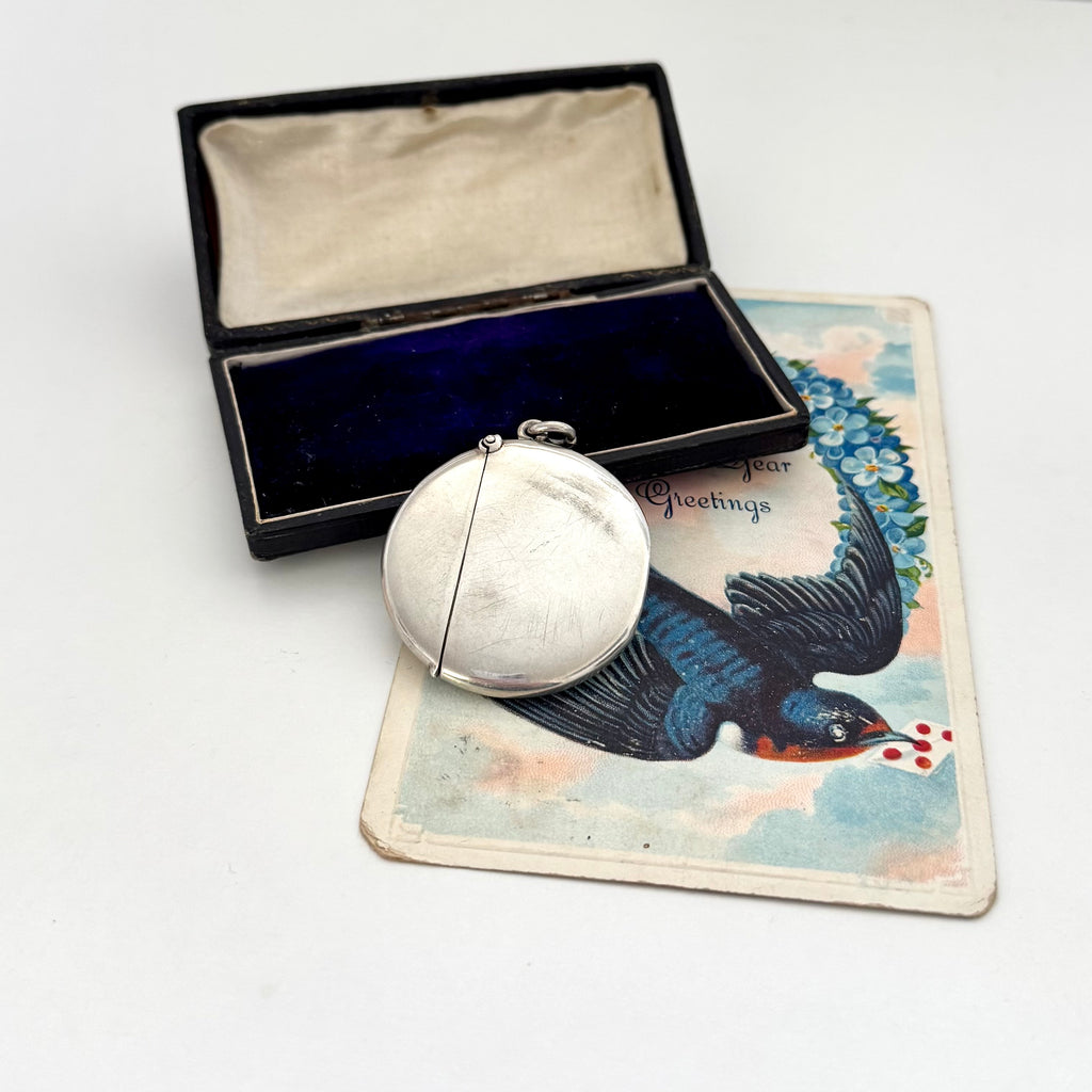 Antique silver round vesta case with a bird design on a vintage card