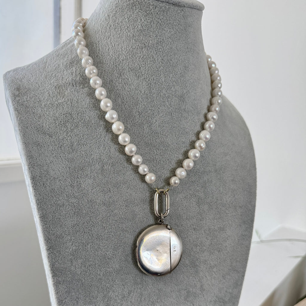 Pearl necklace with a pendant on a gray mannequin bust.