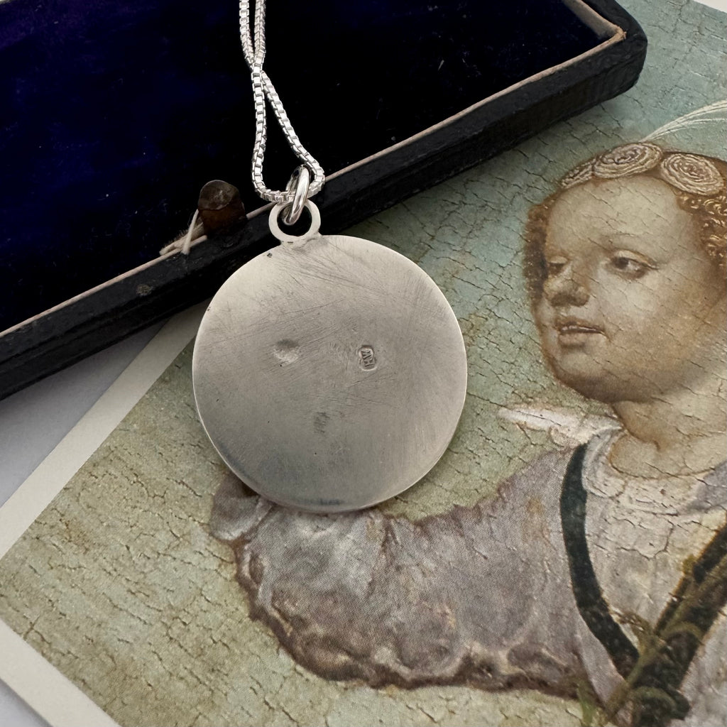 Antique silver pendant necklace on a gray surface with an old book and illustration in the background.
