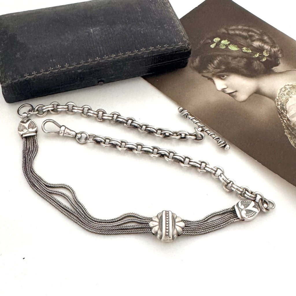 Silver chain with tassels on a white surface next to a black wallet and vintage photo.