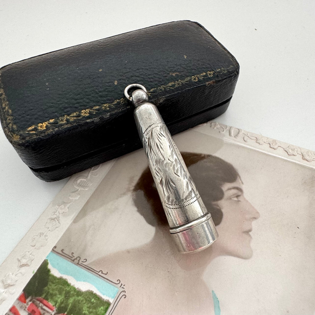 Antique silver cheroot holder case on an old postcard of a woman.