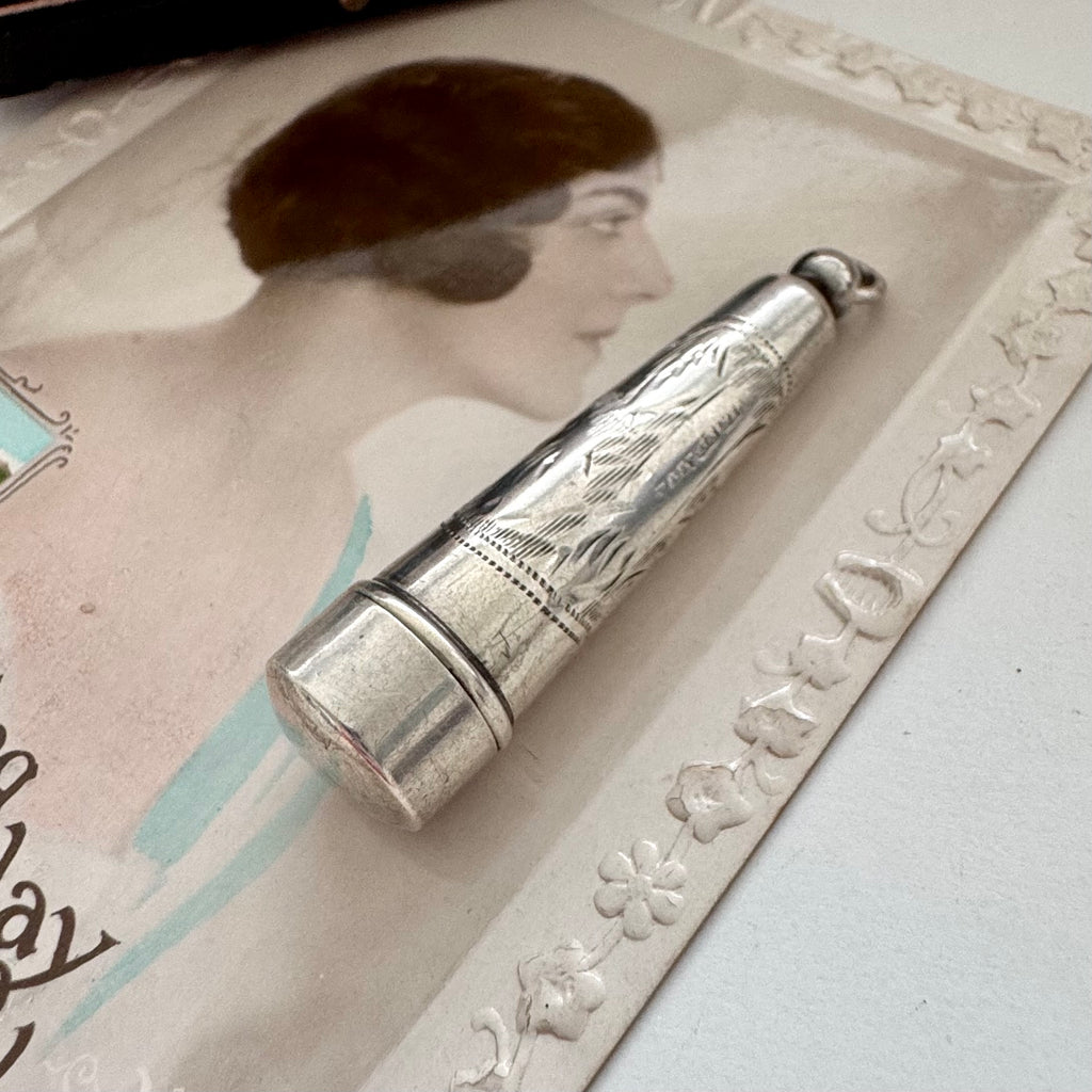 Antique silver cheroot holder case on an old postcard of a woman.