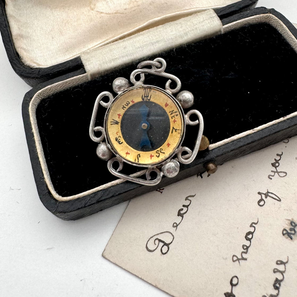 Decorative antique compass in an open box with a vintage card underneath