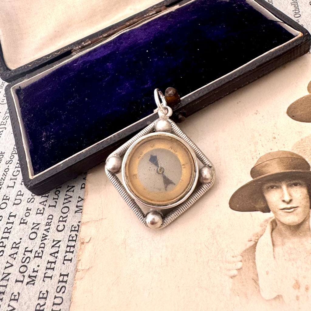 Antique silver compass watch fob with a displayed on an old photograph and text.