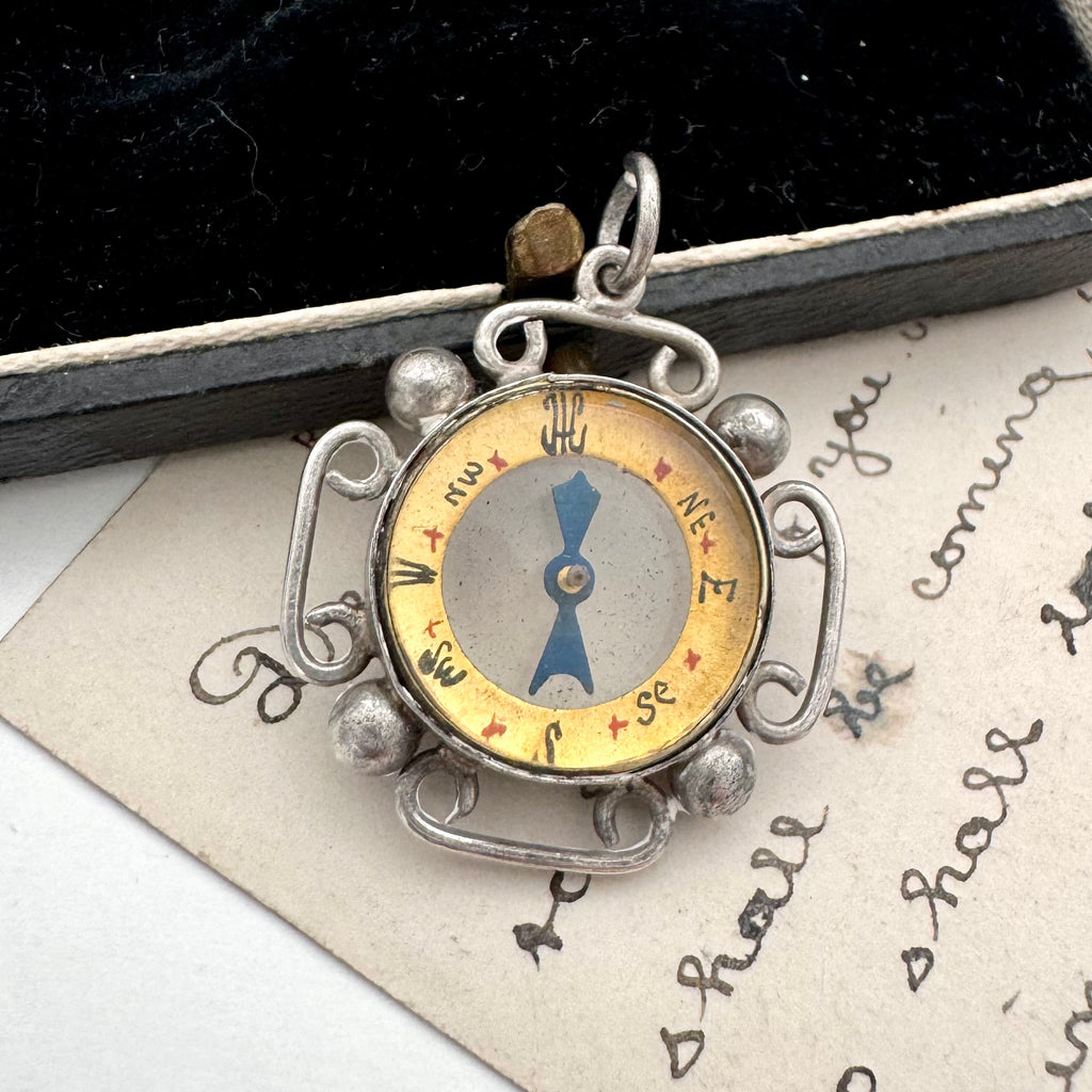 Silver antique compass pendant on a textured surface with text