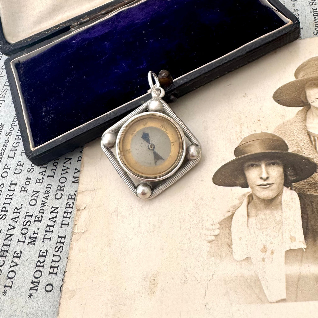 Antique silver compass watch fob with a displayed on an old photograph and text.