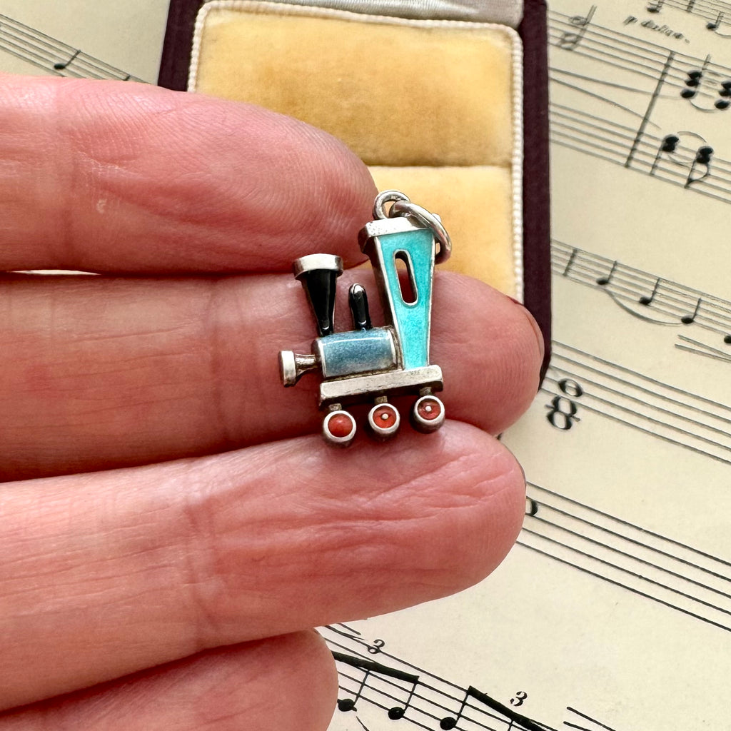 Small antique silver and enamel train charm held between fingers with sheet music in the background