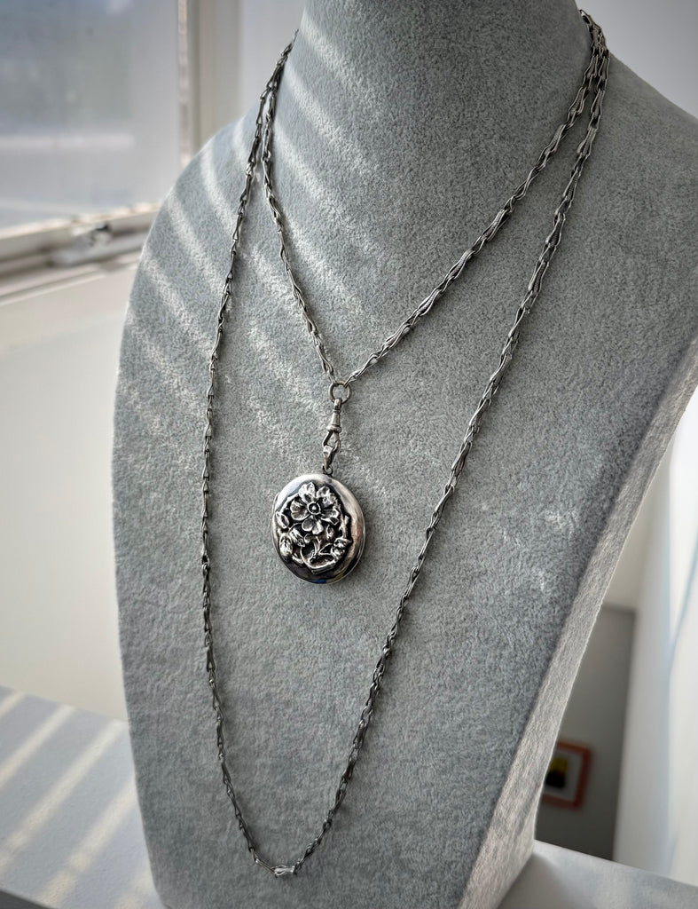 Antique silver fancy link guard chain and silver repousse locket on a grey mannequin