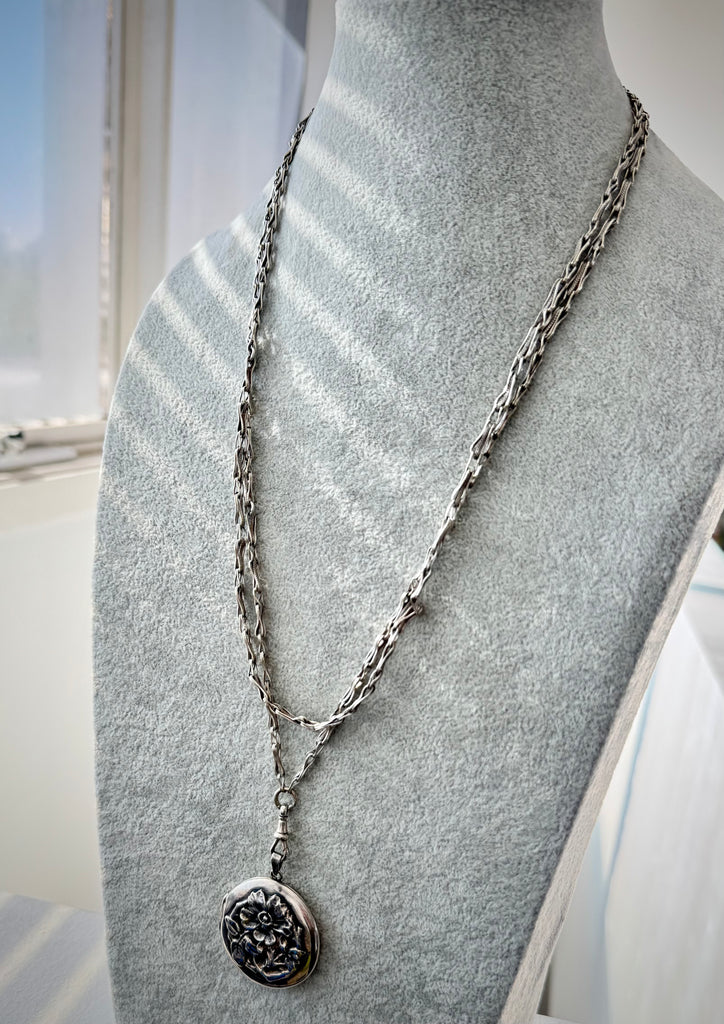 Antique silver fancy link guard chain and silver repousse locket on a grey mannequin