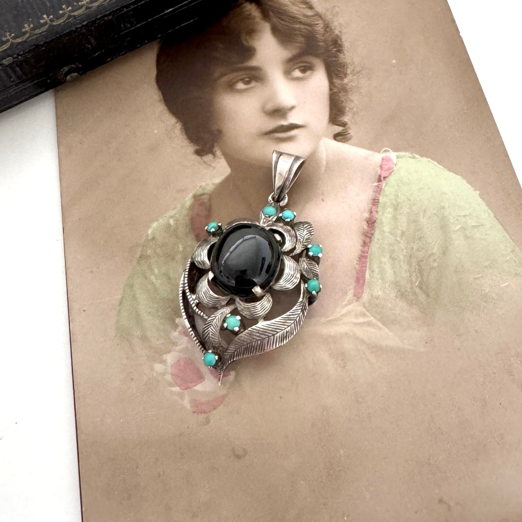 Vintage art nouveau mid century revival necklace with black stone and turquoise stones on a textured surface