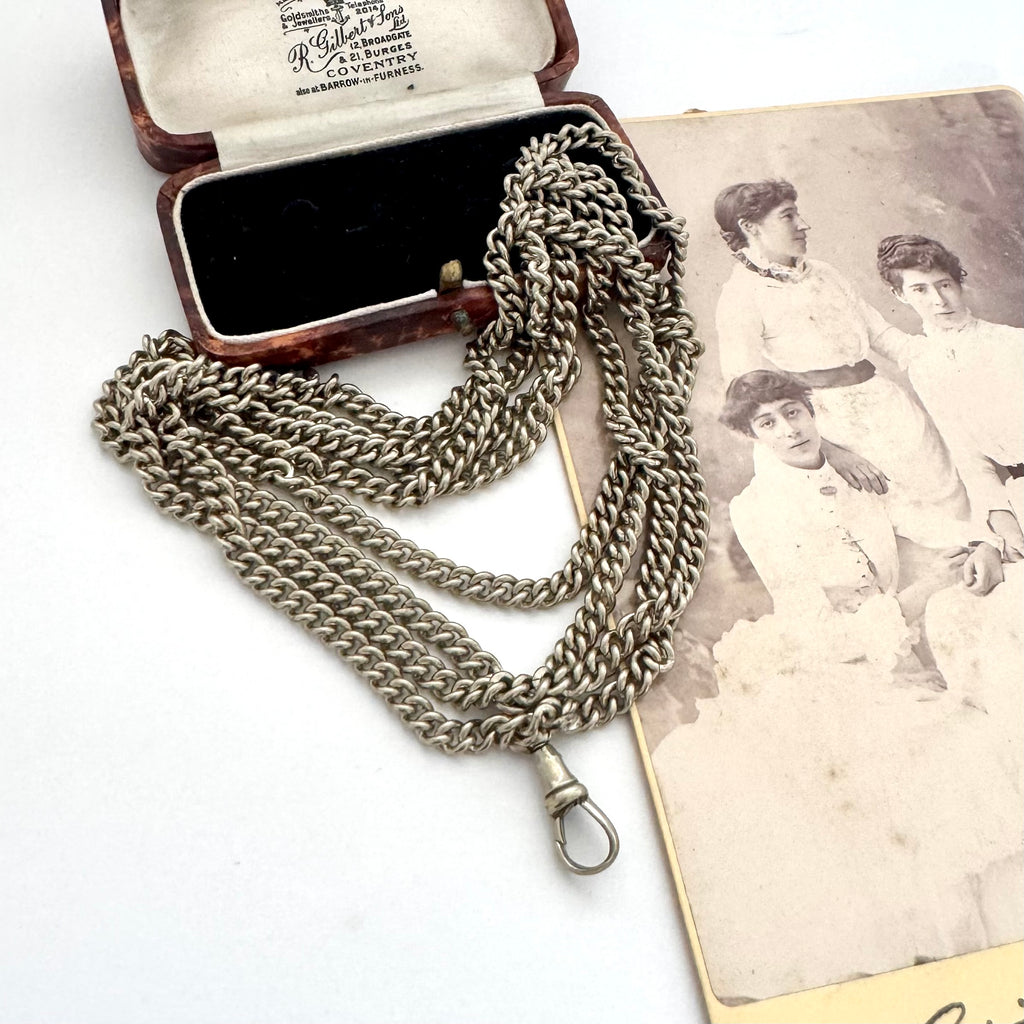 Antique silver plated guard chain necklace with a lobster clasp, displayed next to its open presentation box and a sepia-toned antique photograph on a white background.