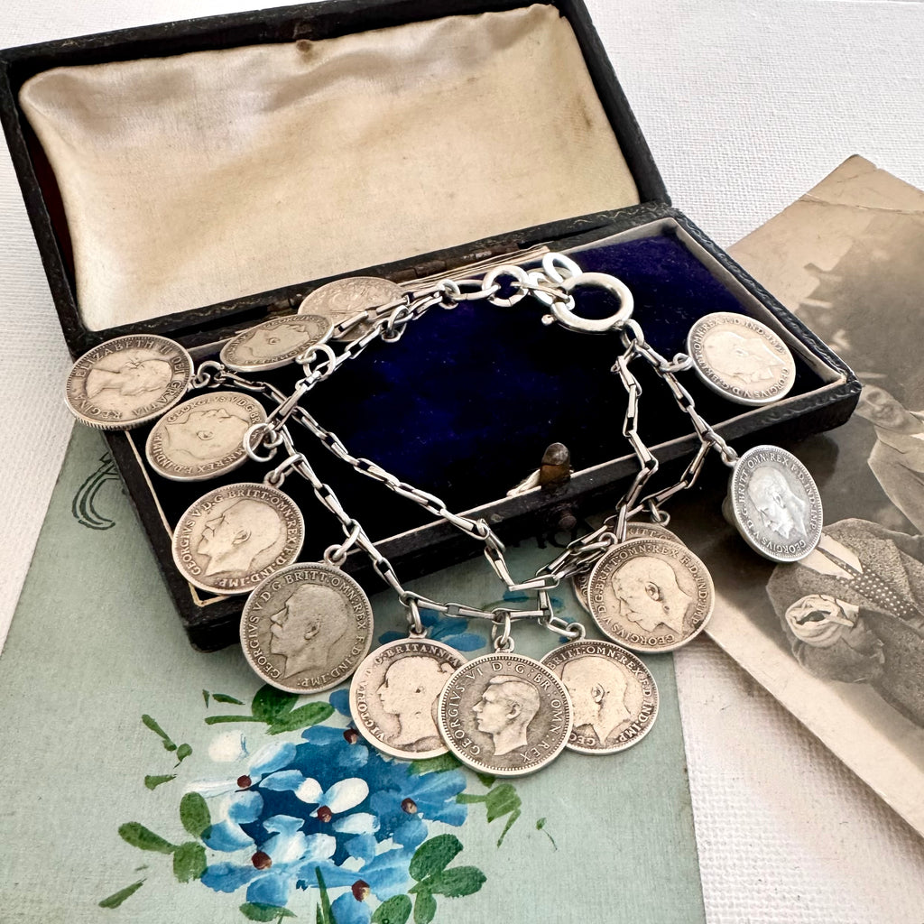 Silver coin bracelet with antique British threepence coins in an open jewelry box on a floral surface.