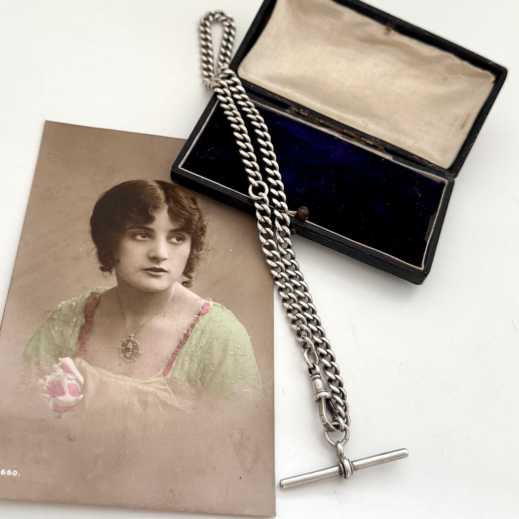 Antique pocket watch chain with an open jewelry box and an old photograph of a woman on a white background.