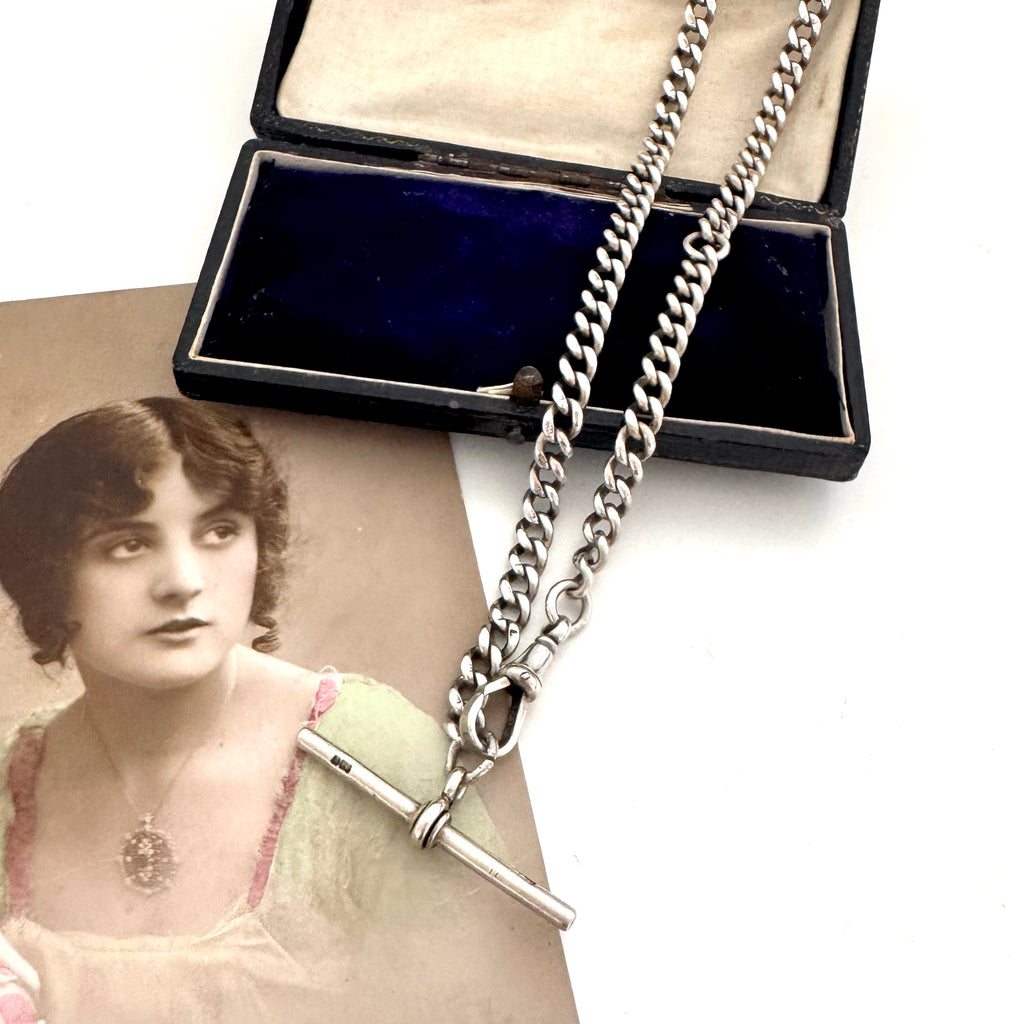 Antique silver watch chain necklace on an old jewellery box and with an old postcard