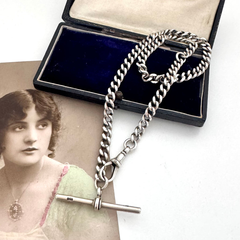 Antique silver watch chain necklace on an old jewellery box and with an old postcard