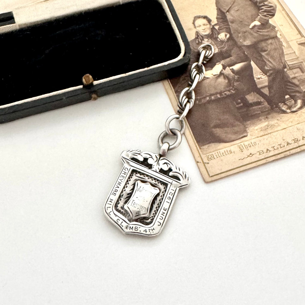 Antique sterling silver watch fob and love knot chain on a white surface next to vintage photograph
