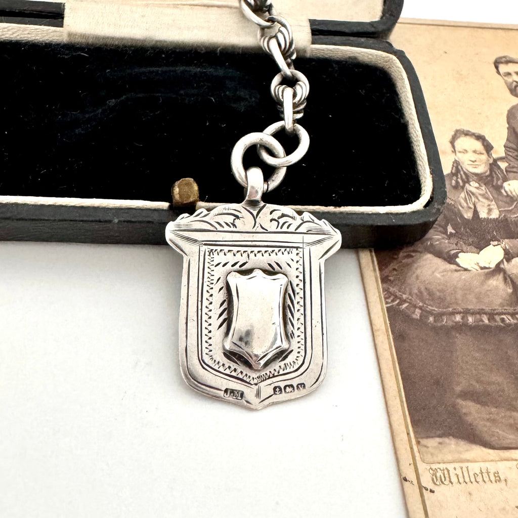 Antique sterling silver watch fob and love knot chain on a white surface next to vintage photograph