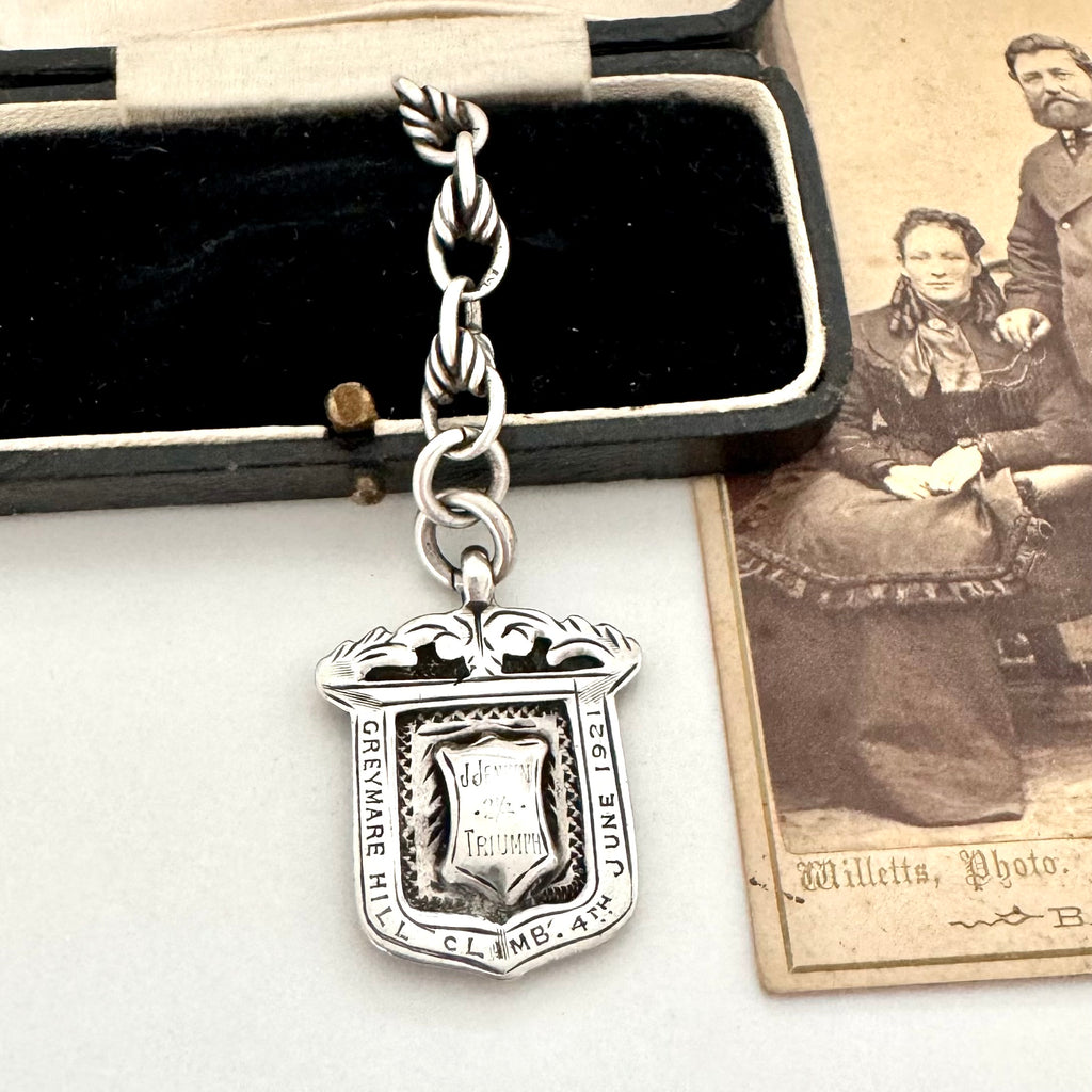 Antique sterling silver watch fob and love knot chain on a white surface next to vintage photograph