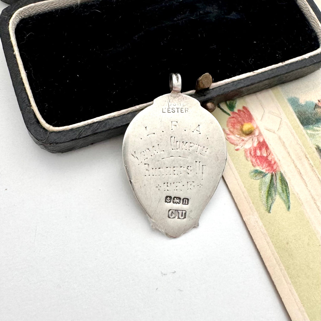 Silver pendant with engraved text on a white surface next to a floral card