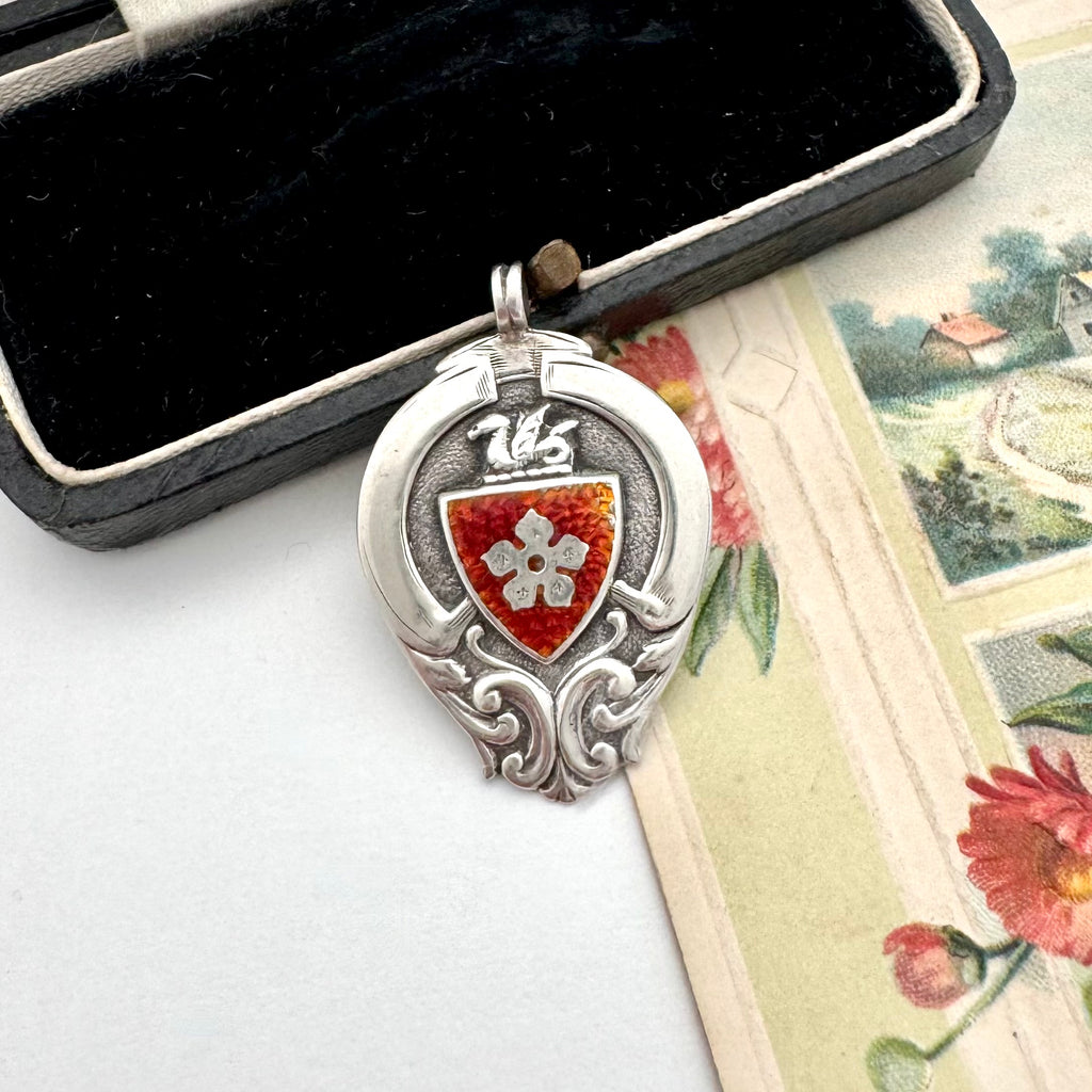 Antique silver and red enamel watch fob on an open jewellery box.