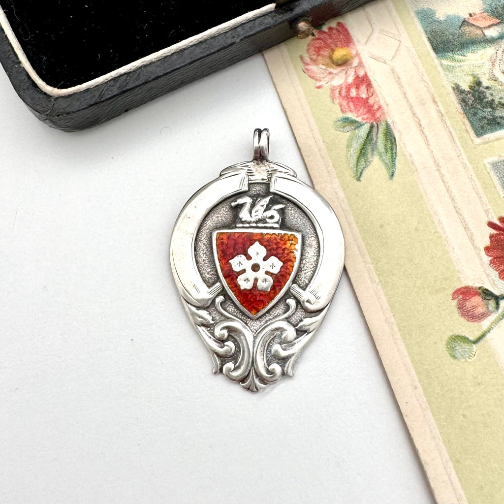 Antique silver and red enamel watch fob on a white background and with a vintage postcard