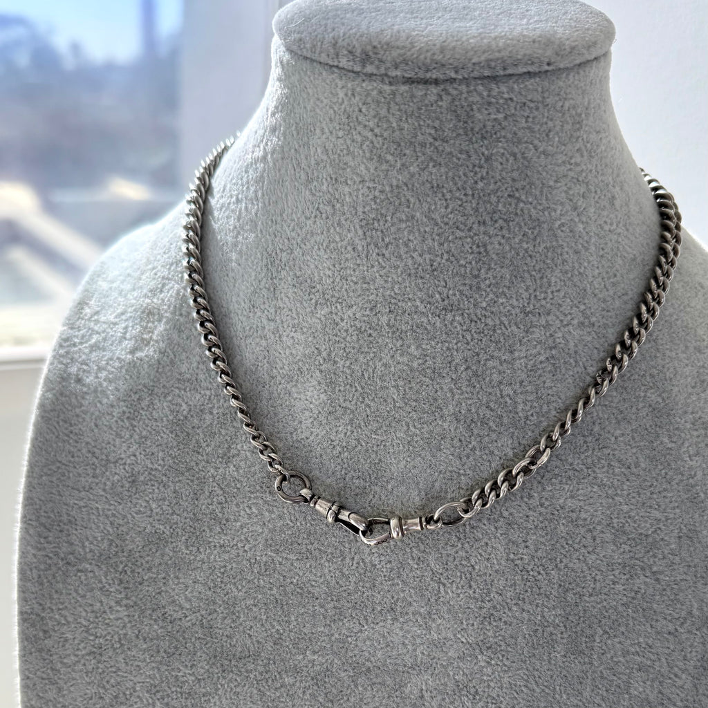 Antique watch chain necklace on a gray mannequin bust with a blurred indoor background