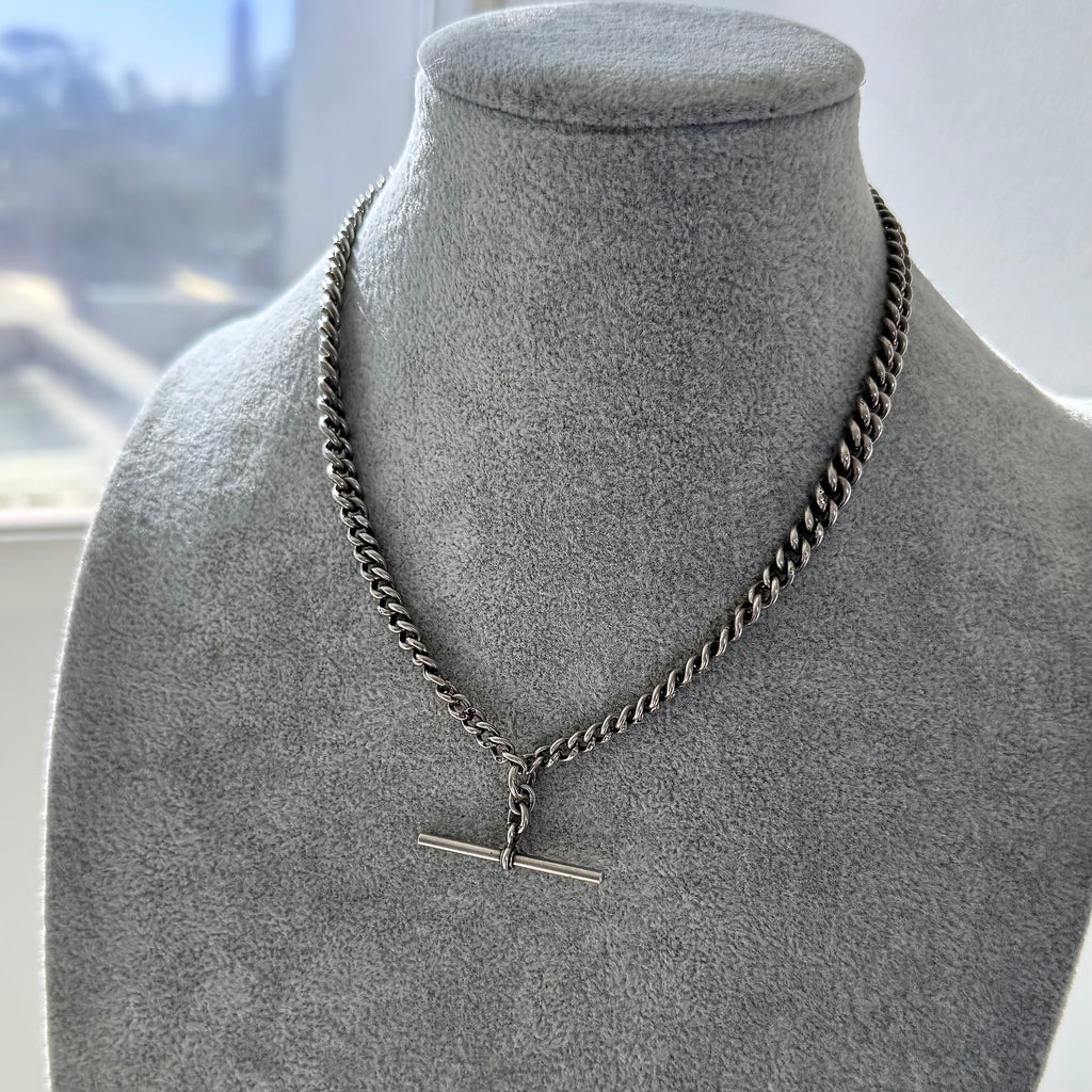 Antique watch chain necklace on a gray mannequin bust with a blurred indoor background