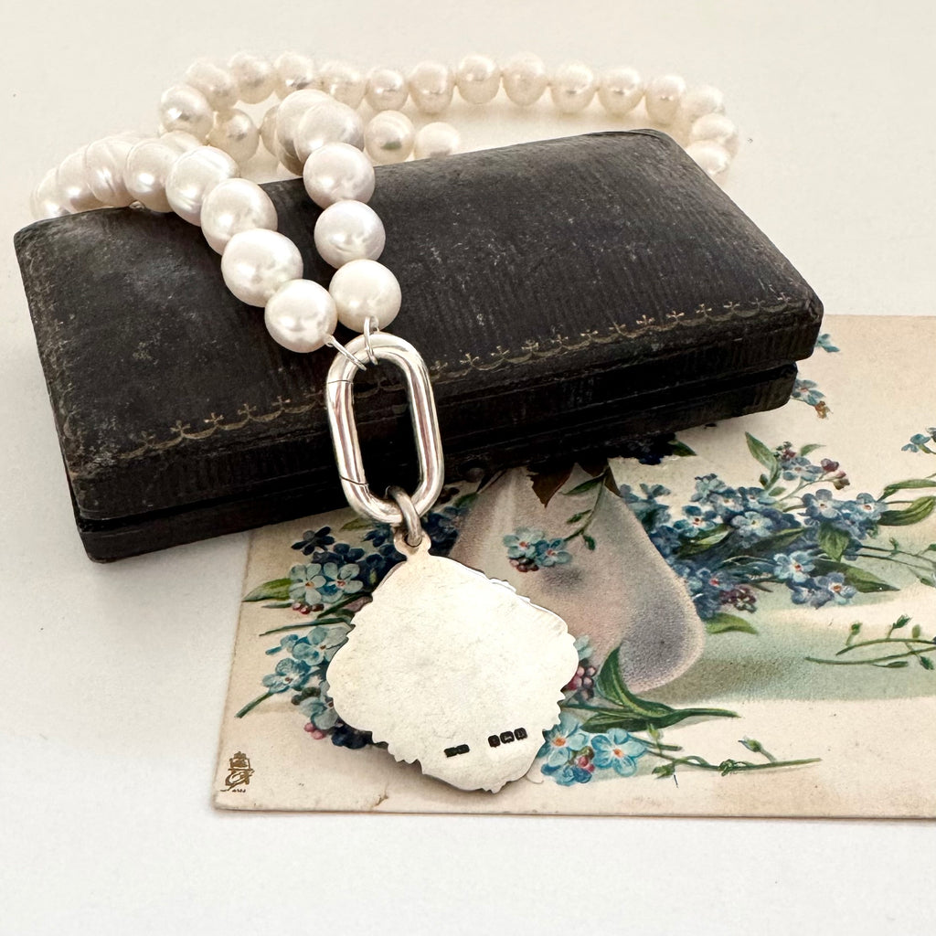 Pearl and antique 1928 watch fob necklace with a silver clasp on a jewellery box with floral card in the background