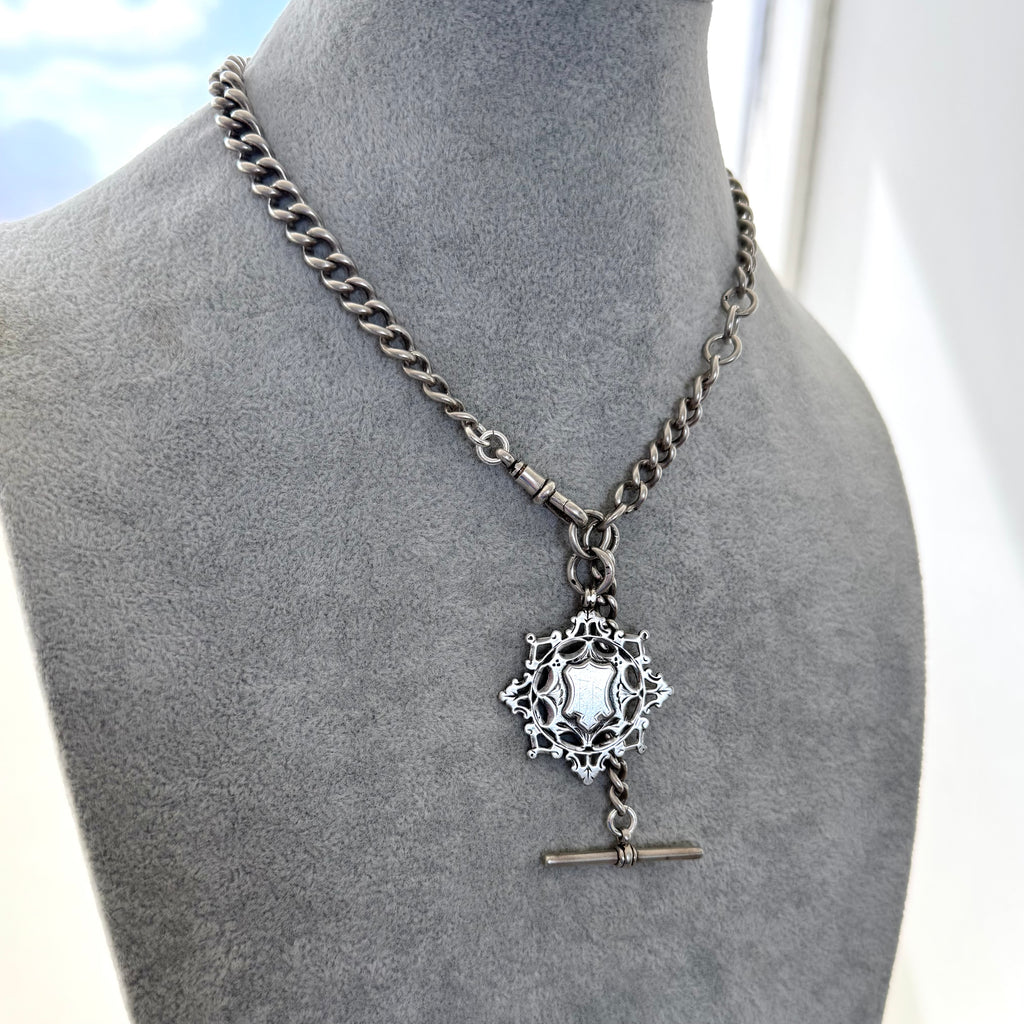 Antique silver albert watch chain and watch fob necklace with an albert clasp on a grey mannequin.