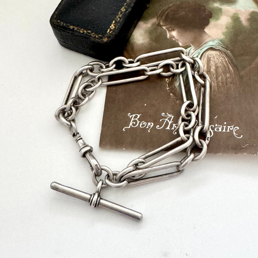 Antique silver trombone chain bracelet on a white surface with a vintage-style card in the background.