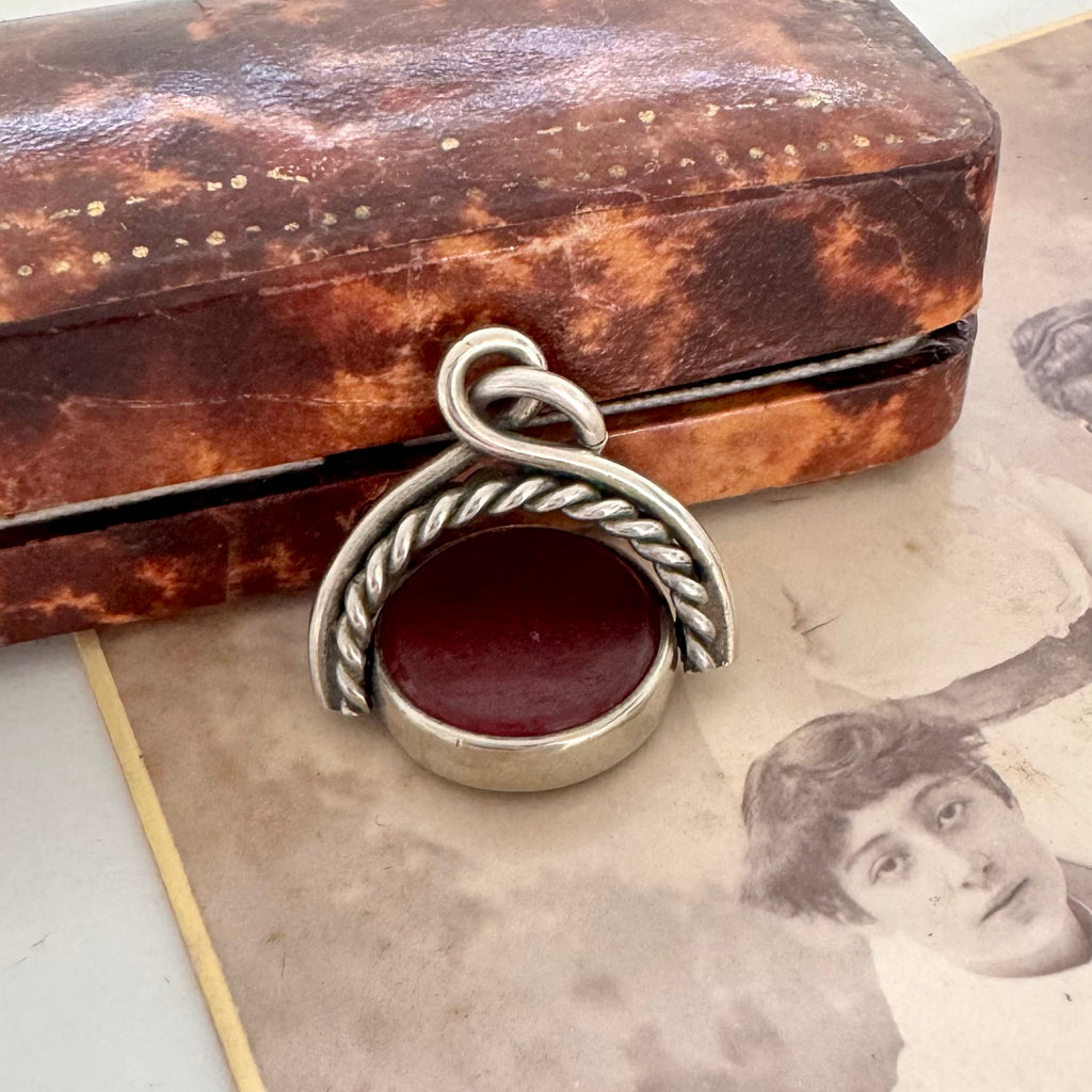 Antique victorian albo silver carnelian and bloodstone spinning fob displayed on top of a vintage sepia-toned photograph and a vintage jewellery box.
