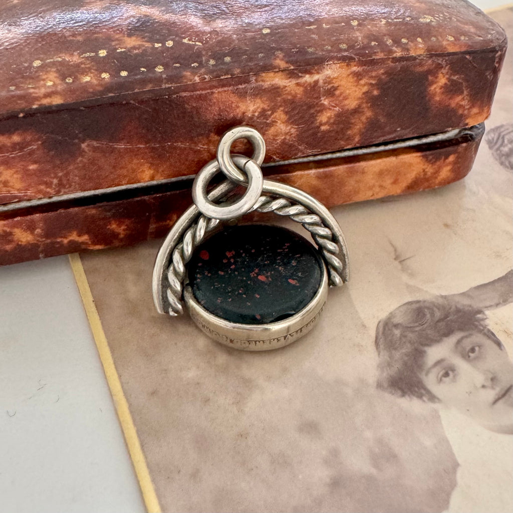 Antique victorian albo silver carnelian and bloodstone spinning fob displayed on top of a vintage sepia-toned photograph and vintage jewellery box.