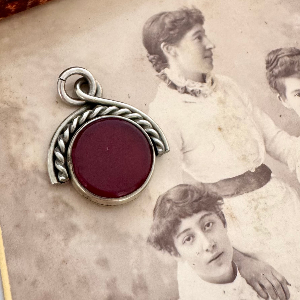A Victorian albo silver spinning fob with a round deep red center, placed on top of an old sepia-toned photograph of two women.
