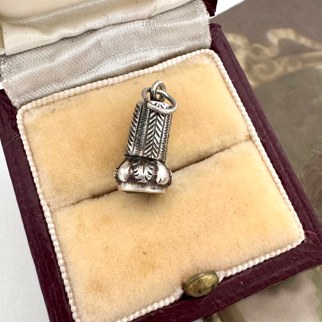 An antique silver wax seal fob charm pendant with engraved leaf and chevron patterns, displayed inside an open vintage burgundy velvet jewelry box with cream velvet lining.