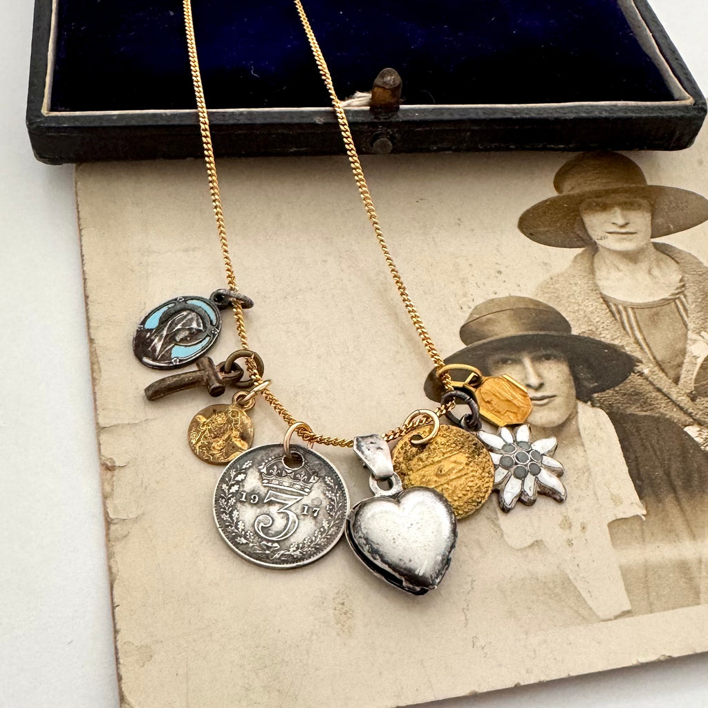A collection of antique and vintage charms on a gold chain and on an antique photograph of three women wearing hats.