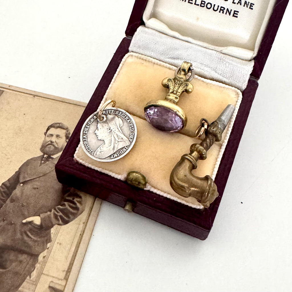 Antique jewelry set with a pendant and brooch in an open jewelry box, next to a vintage photograph.