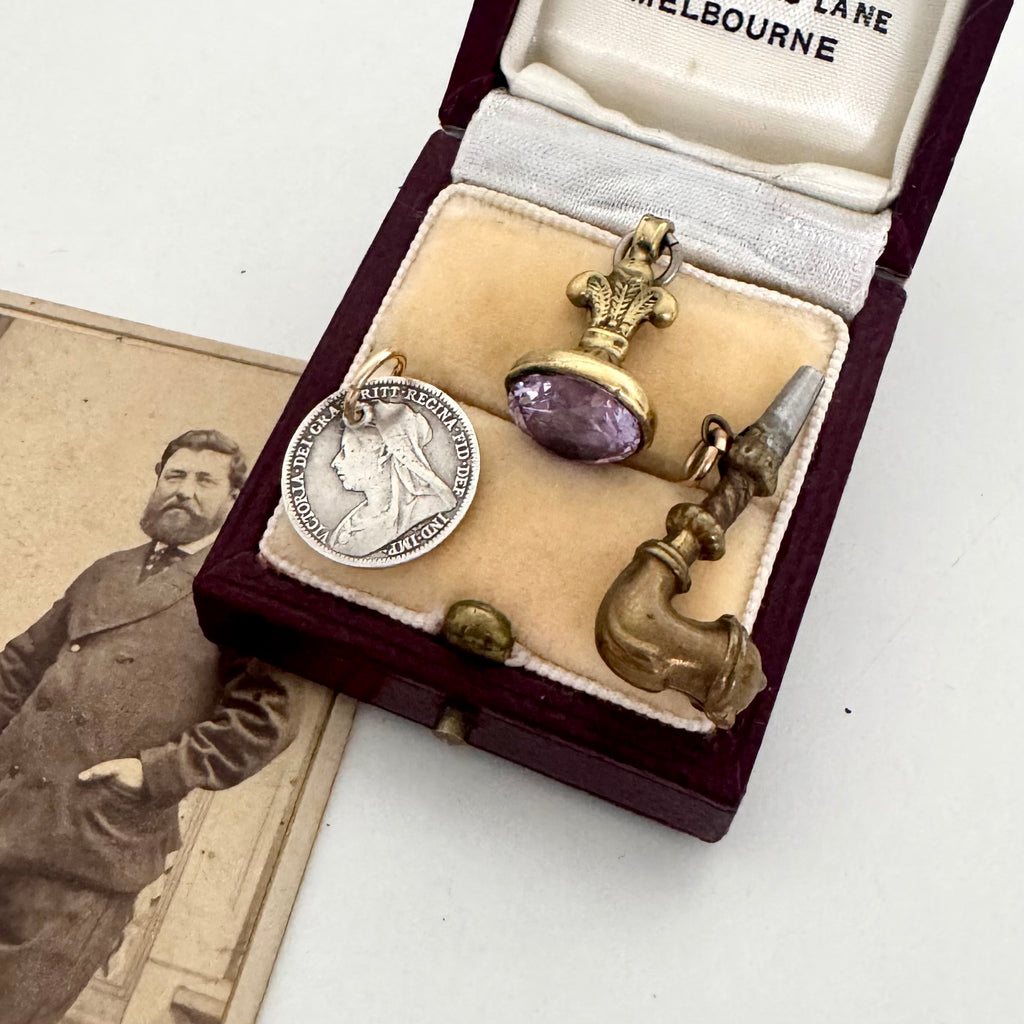 Antique jewelry set with a pendant and brooch in an open jewelry box, next to a vintage photograph.