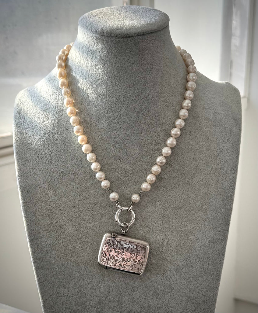 Pearl necklace with a silver antique vesta case pendant on a gray mannequin bust.