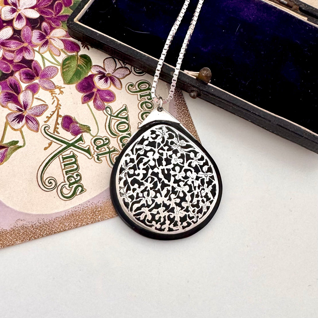 Antique silver and tortoiseshell pendant on a decorative card with floral design