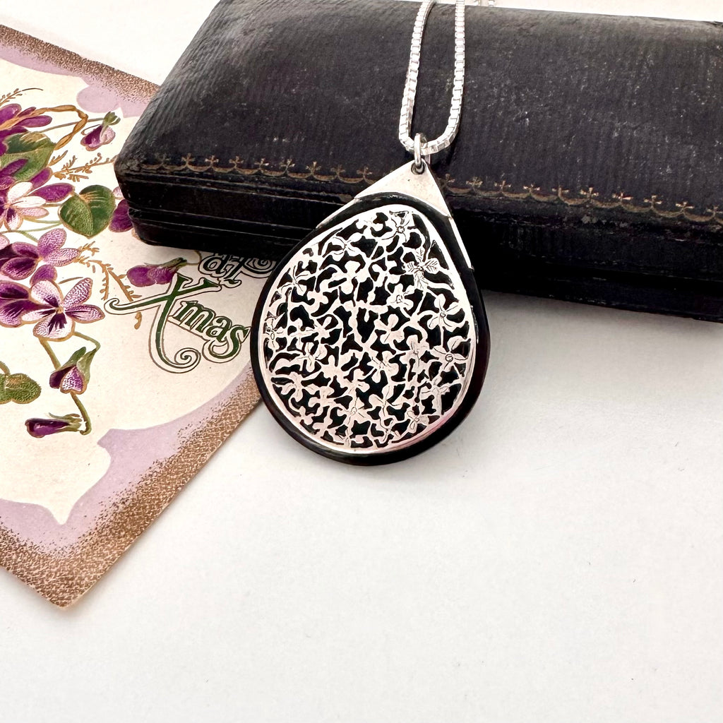 Antique silver and tortoiseshell pendant on a decorative card with floral design