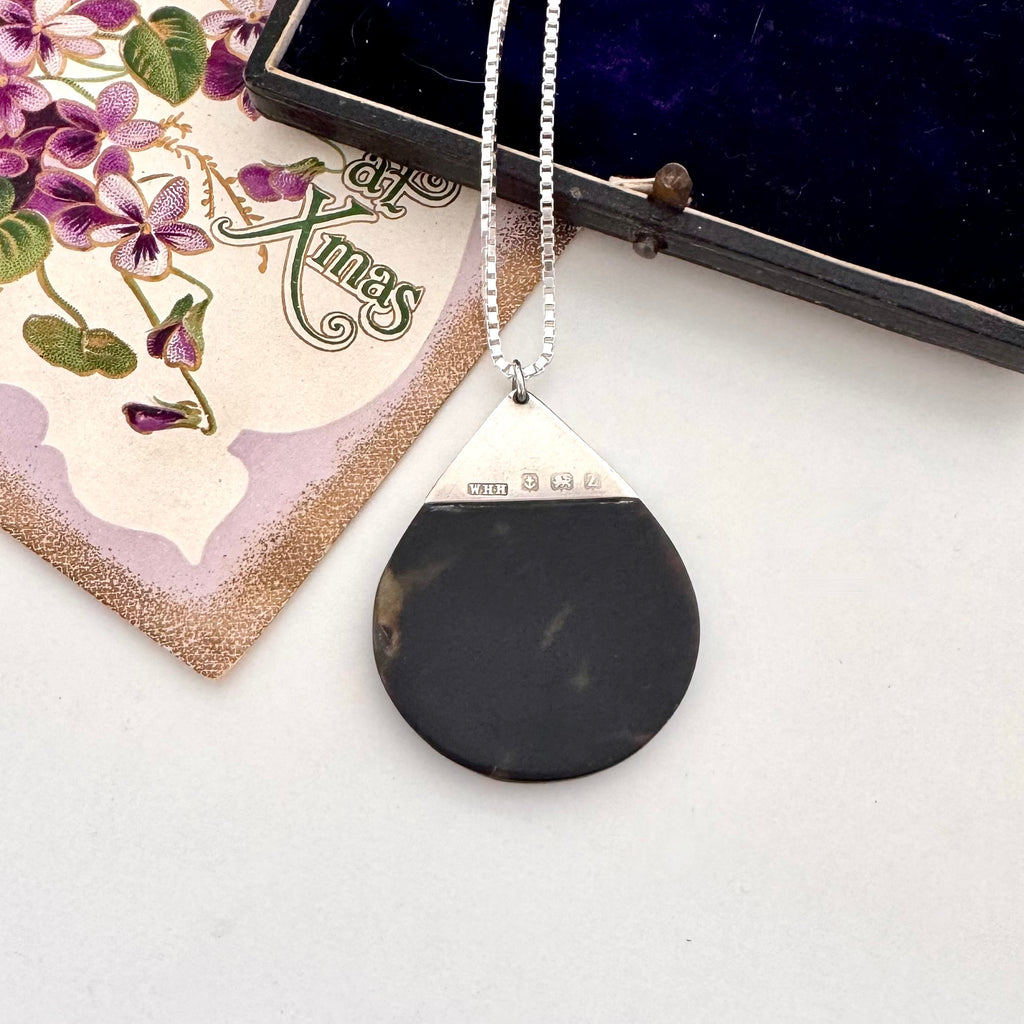 Antique silver and tortoiseshell pendant on a decorative card with floral design