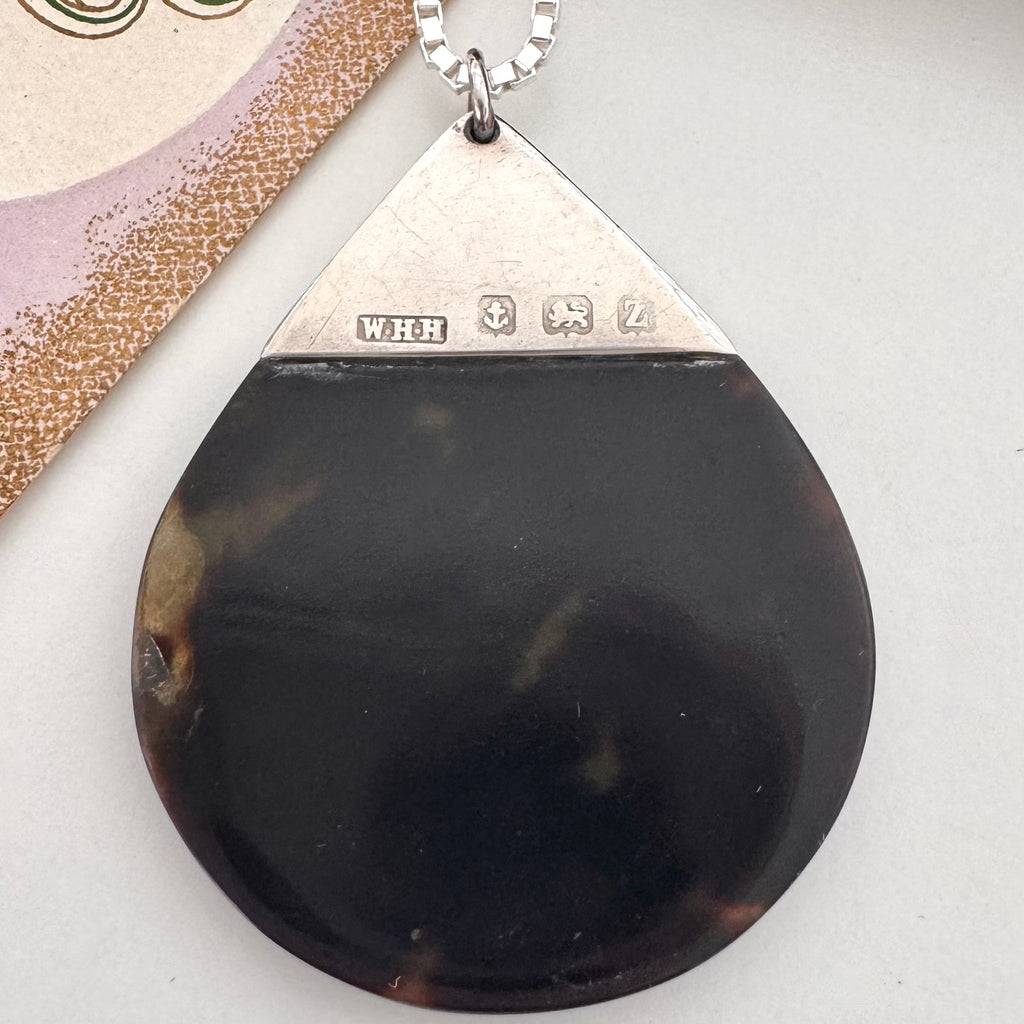 Antique silver and tortoiseshell pendant on a decorative card with floral design
