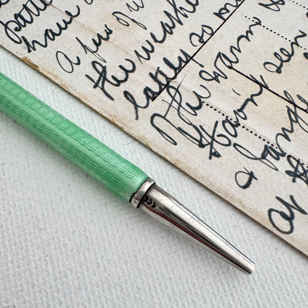 Art Deco silver and guilloche enamel propelling pencil resting on a textured white surface next to a piece of vintage handwritten paper.
