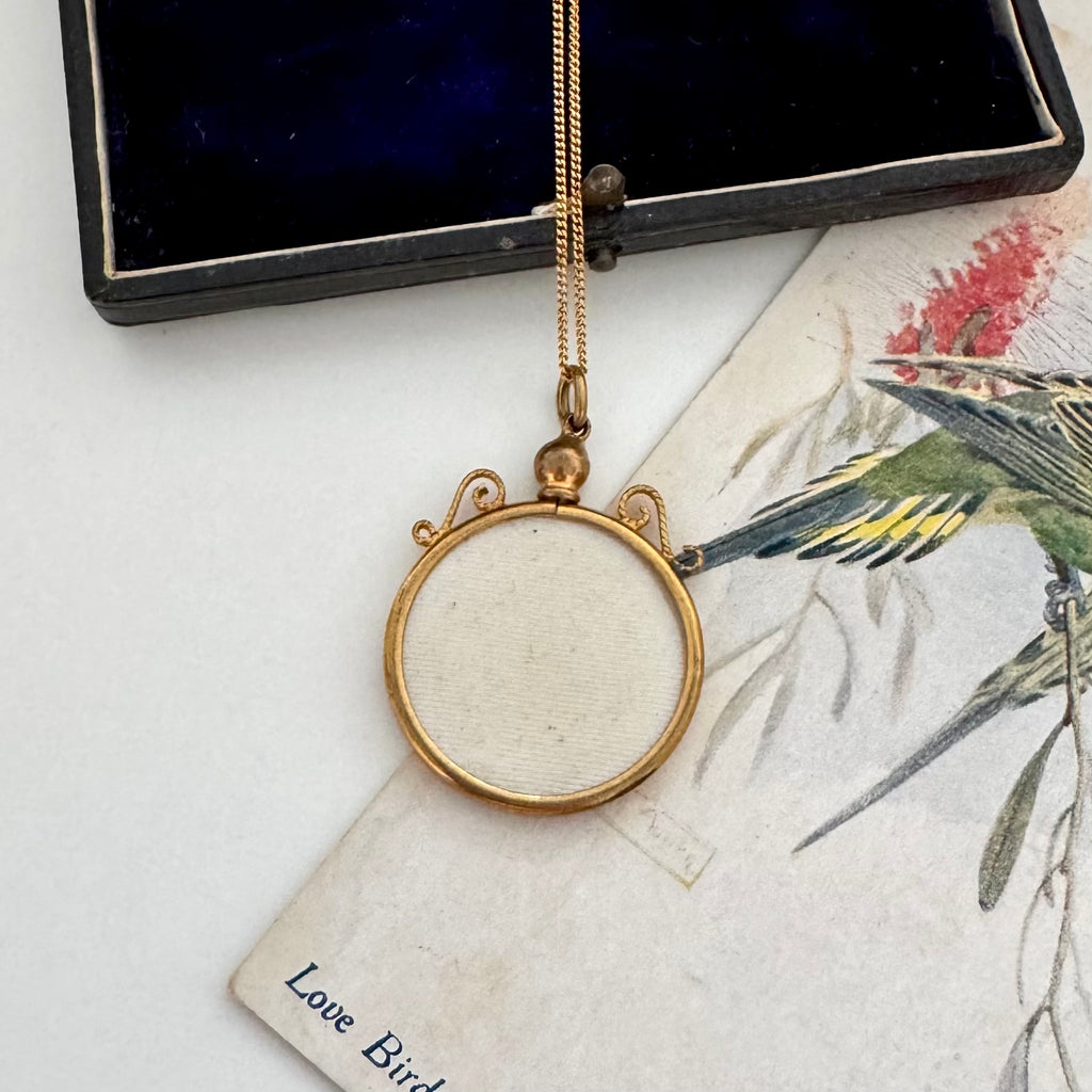 Gold necklace with a round pendant on a vintage-style card with bird illustration