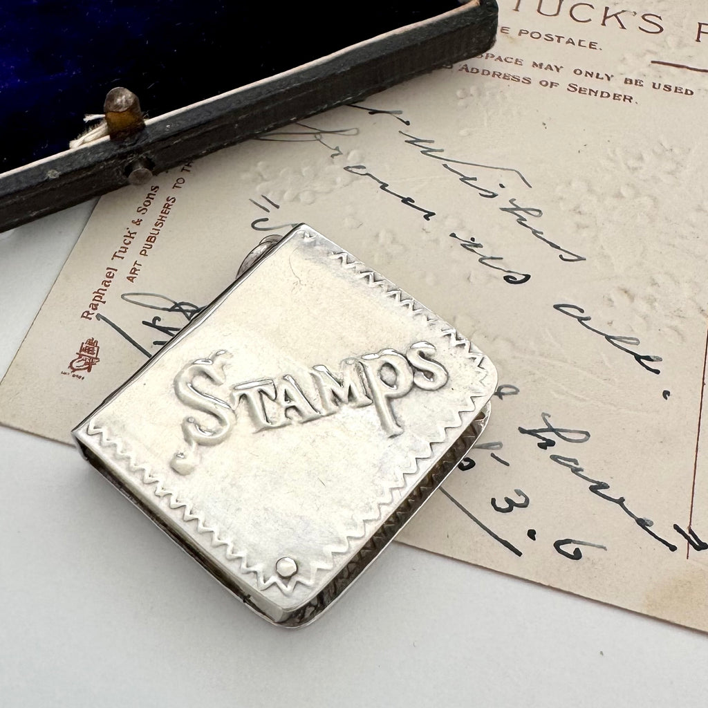 Silver stamp holder with 'STAMPS' engraved on it, placed on an old letter.