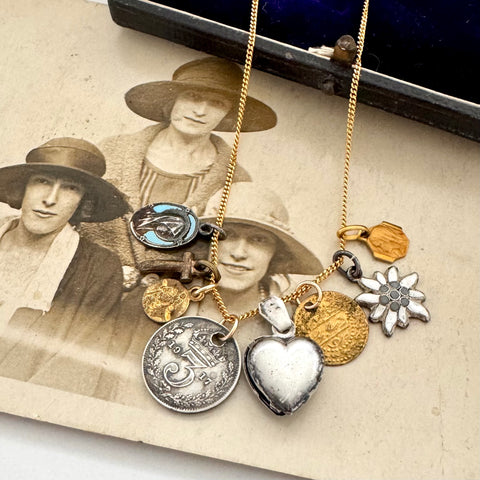 A collection of antique and vintage charms on a gold chain and on an antique photograph of three women wearing hats.