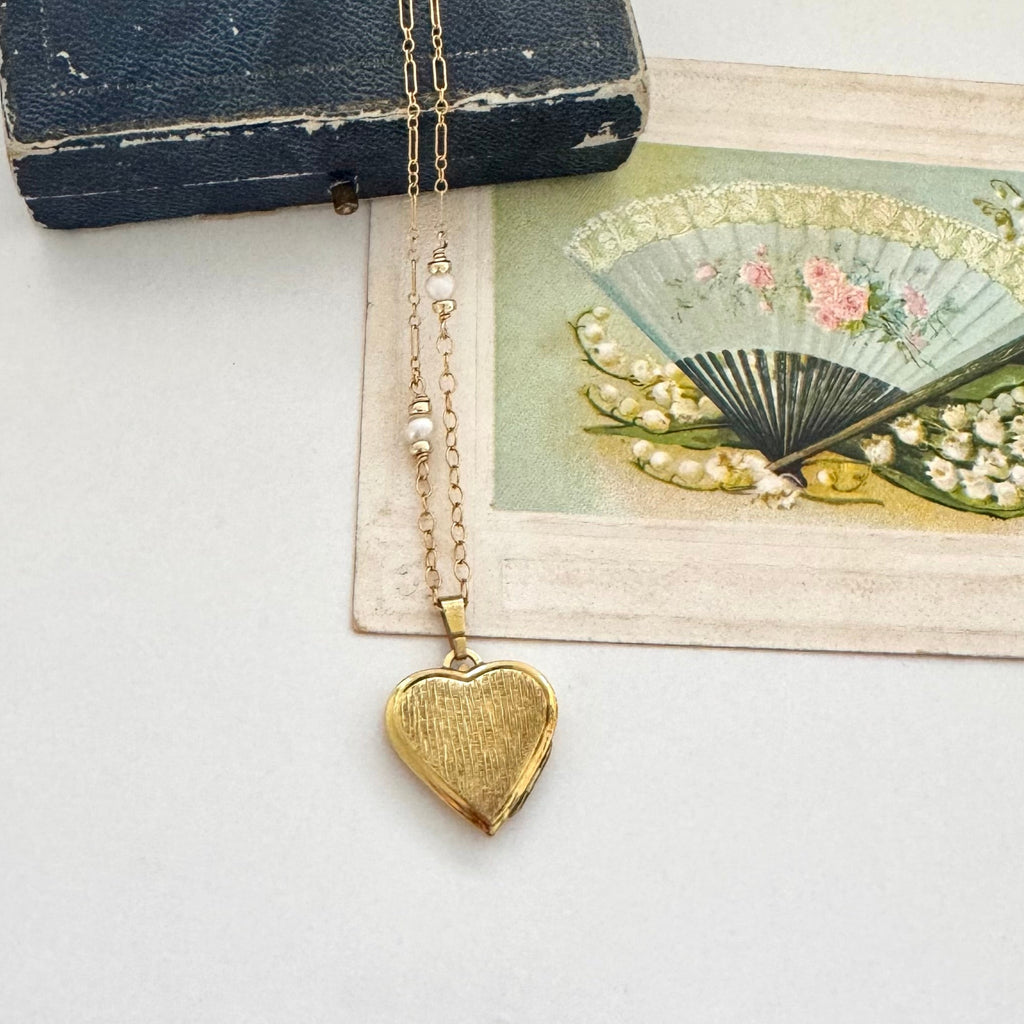 Gold heart-shaped pendant necklace on a vintage-style card with a fan design.