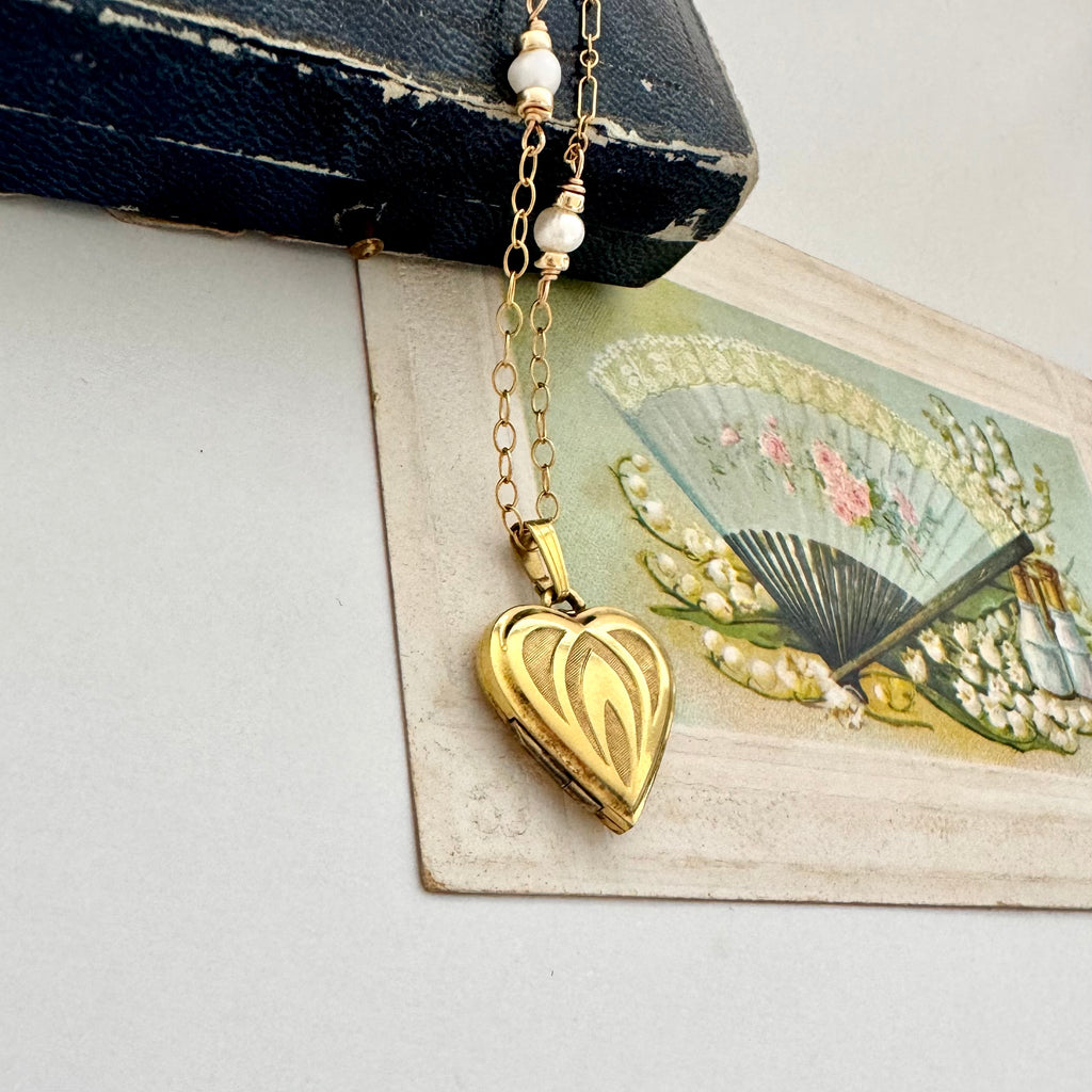 Gold heart-shaped locket necklace on an old box with floral and fan postcard
