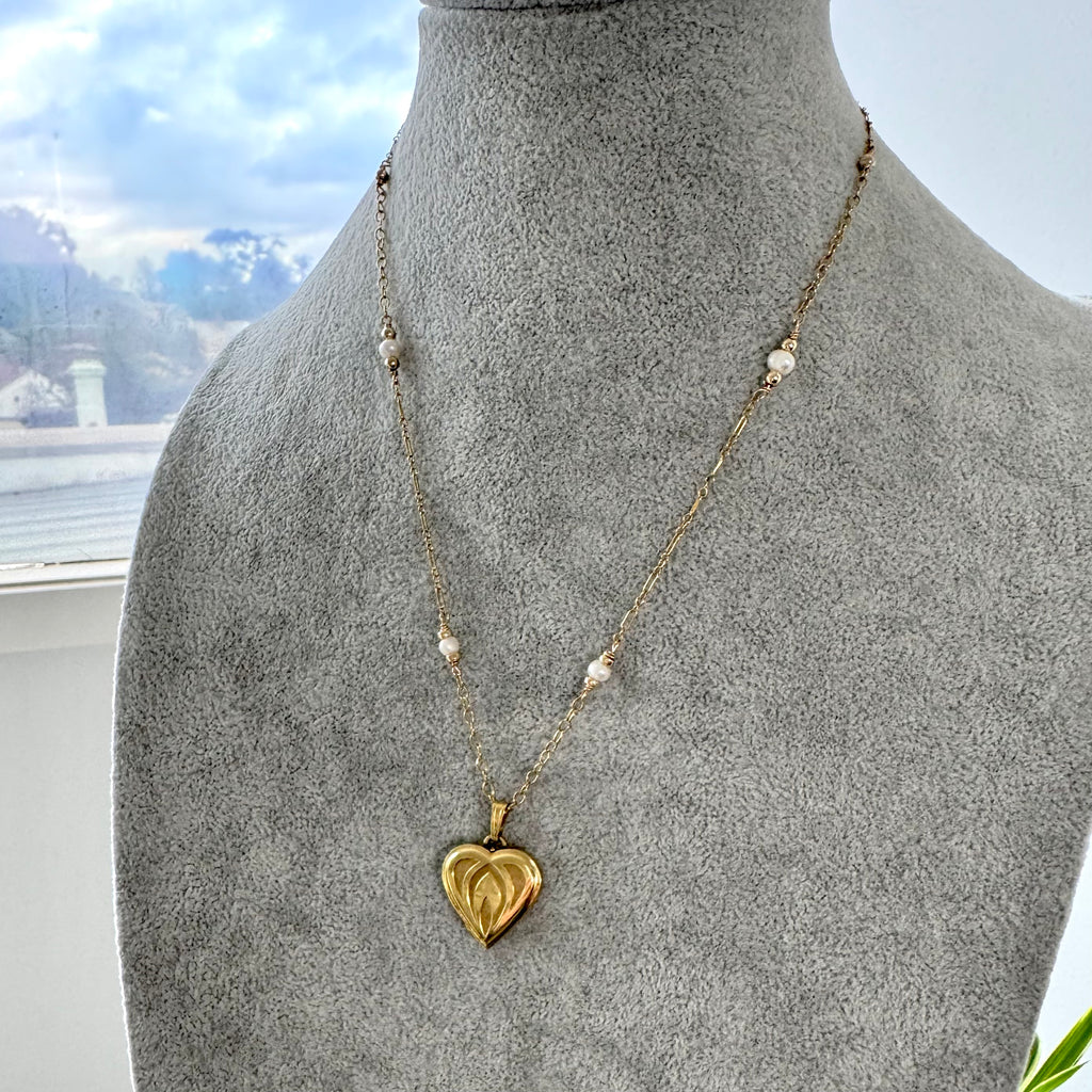 Gold heart-shaped pendant necklace on a mannequin with a scenic background