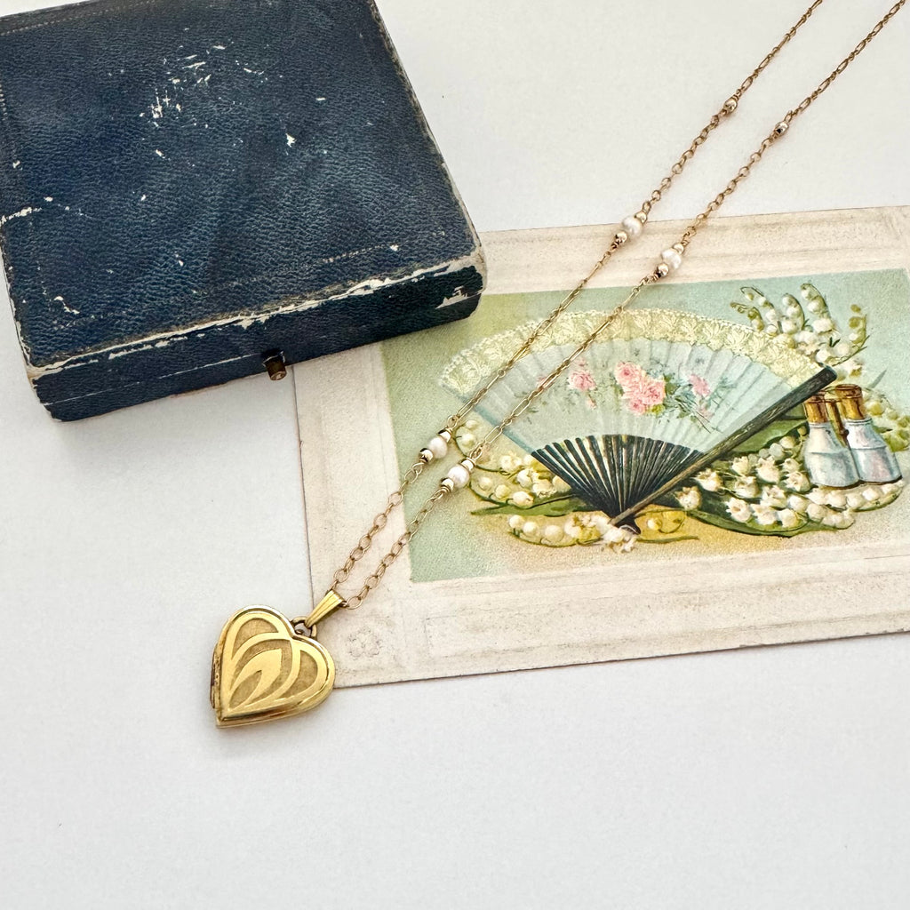 Heart-shaped locket necklace on a vintage-style card with a fan and bottles.